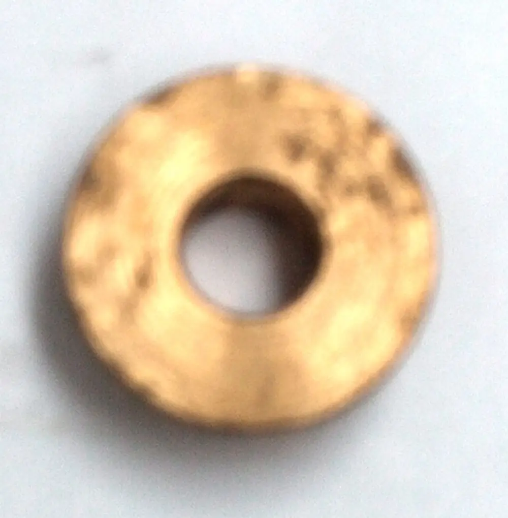 Braunes, flaches Metallteil mit zentralem Loch, möglicherweise eine Gasdichtung oder Membran von Daikin, auf hellem Hintergrund.